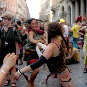 A color photograph capturing costumed participants dancing energetically in a cobblestone street during the Par tòt Parata parade in Bologna, Italy, on June 9, 2007.