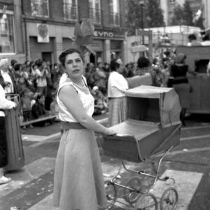 Black and white photo of a participant dressed in a vintage 1950s style costume pushing a retro pram during the Zinneke Parade 2012 in Brussels, Belgium.