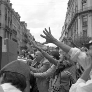 Black and white photo of an enthusiastic crowd shouting and reaching out towards cardboard boxes during a street performance at the Zinneke Parade 2012 in Brussels.